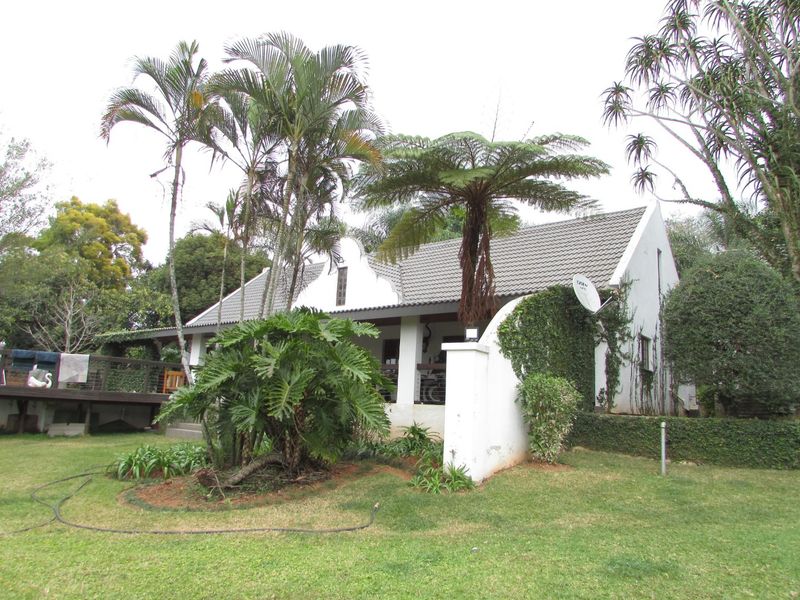 Rear view of a house featuring a tiled roof, a covered patio, and a raised timber deck set within a mature landscaped garden.