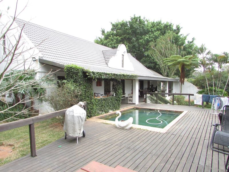 Outdoor entertainment area featuring a swimming pool and timber decking, set against a traditional home with a covered patio and established garden.