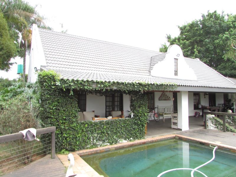 Rear view of the property featuring a covered patio area, timber decking, and a swimming pool set against a gabled roof structure.