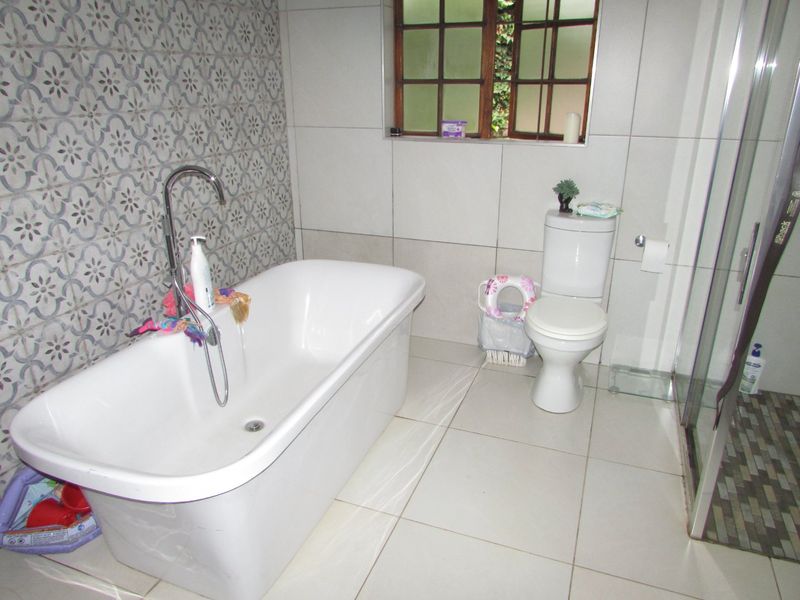 A modern bathroom featuring a freestanding bathtub with floor-mounted mixer, a separate shower enclosure, and a combination of neutral and patterned feature wall tiles.
