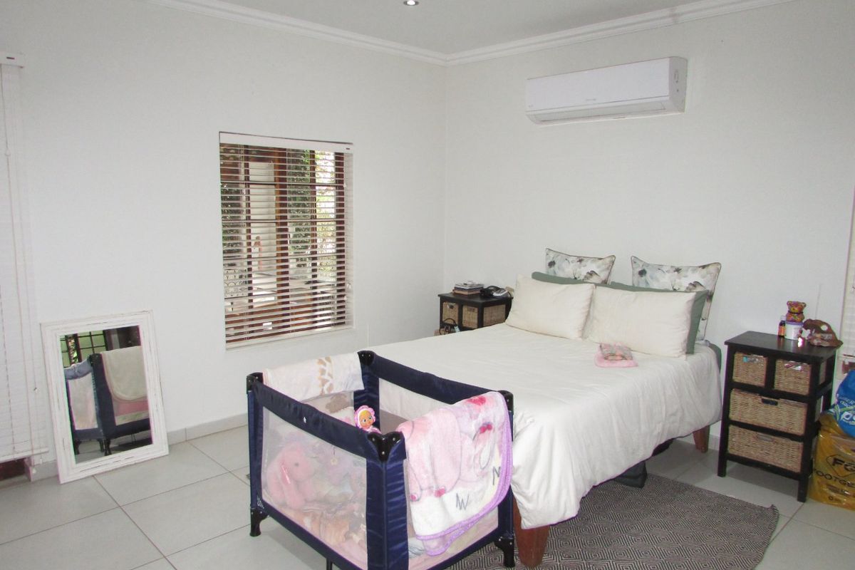 A well-maintained bedroom featuring tiled flooring, recessed downlighting, an air conditioning unit, and venetian blinds.
