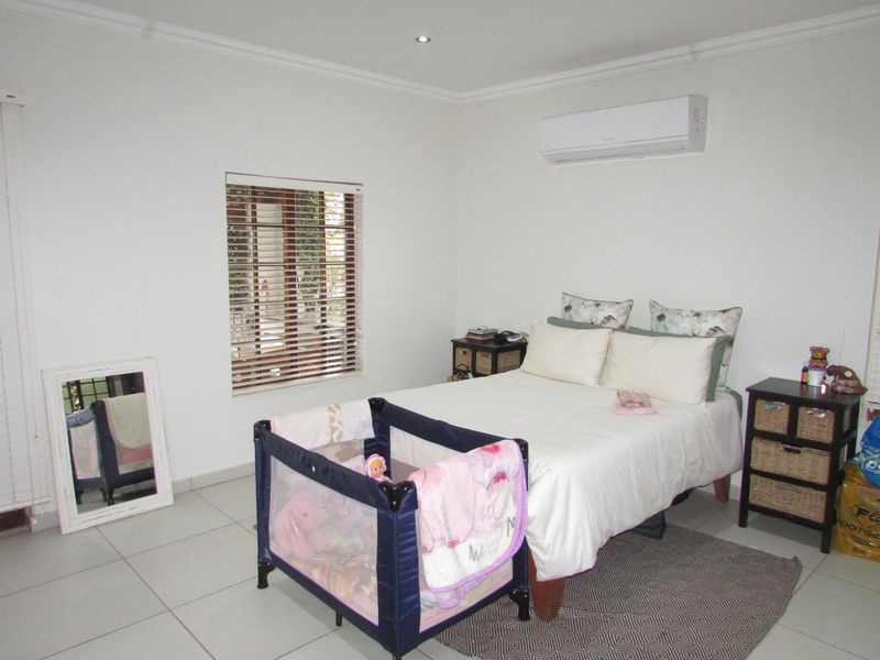 A well-maintained bedroom featuring tiled flooring, recessed downlighting, an air conditioning unit, and venetian blinds.
