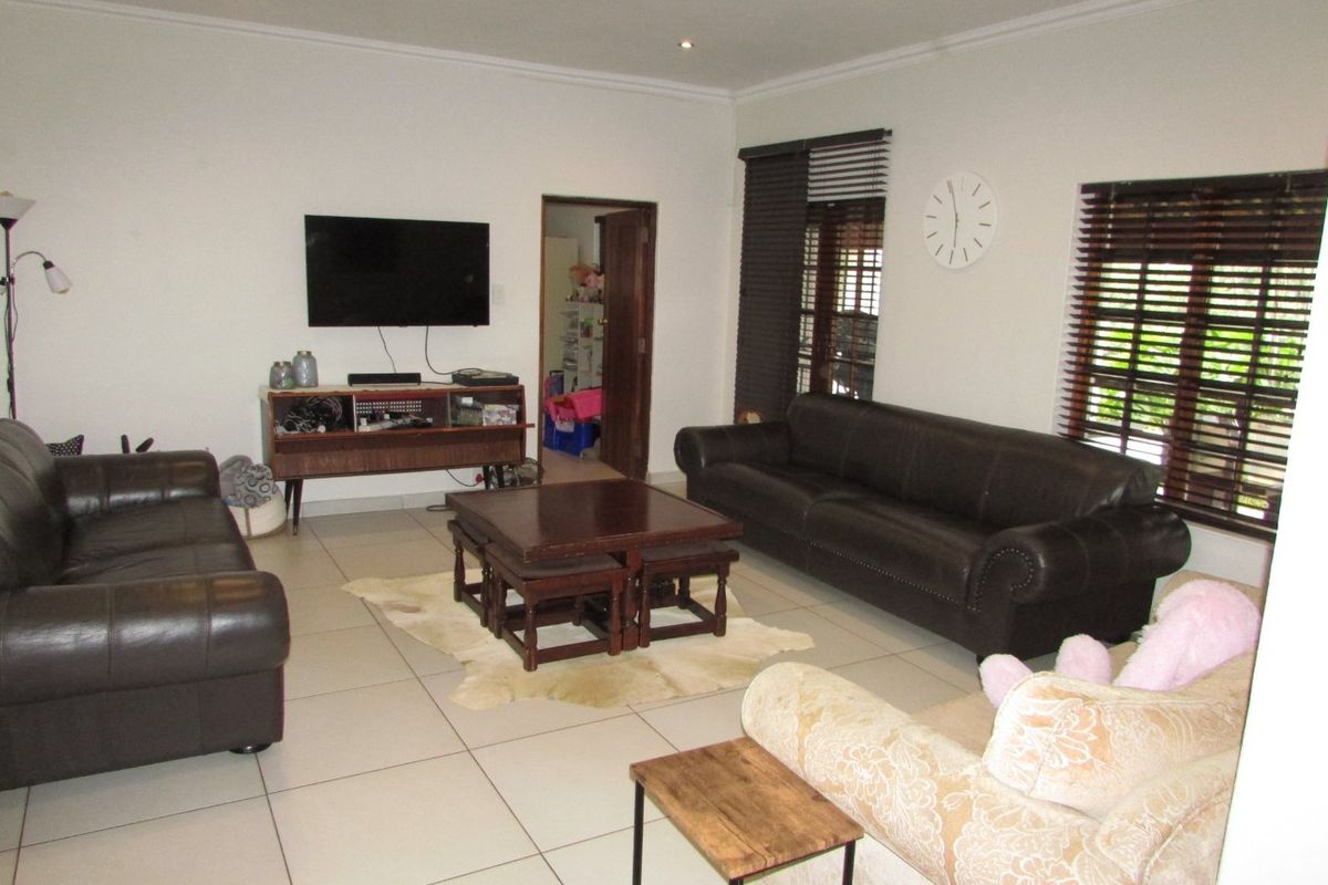 Spacious living room featuring neutral tiled flooring, recessed downlighting, and large windows fitted with venetian blinds.