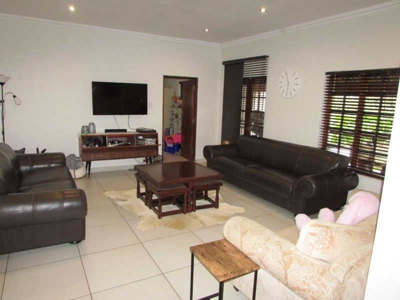 Spacious living room featuring neutral tiled flooring, recessed downlighting, and large windows fitted with venetian blinds.