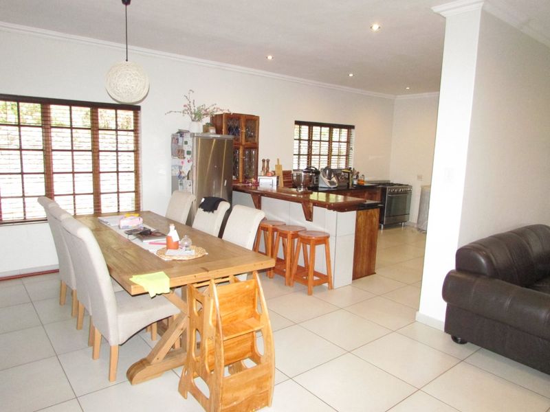 Open plan living and dining area featuring tiled flooring, recessed lighting, and a functional kitchen with a breakfast bar and timber window frames.