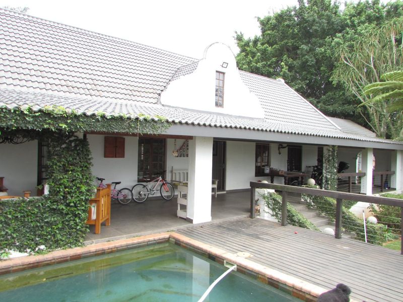 A covered patio area overlooking a swimming pool with timber decking and a traditional gabled roof structure.