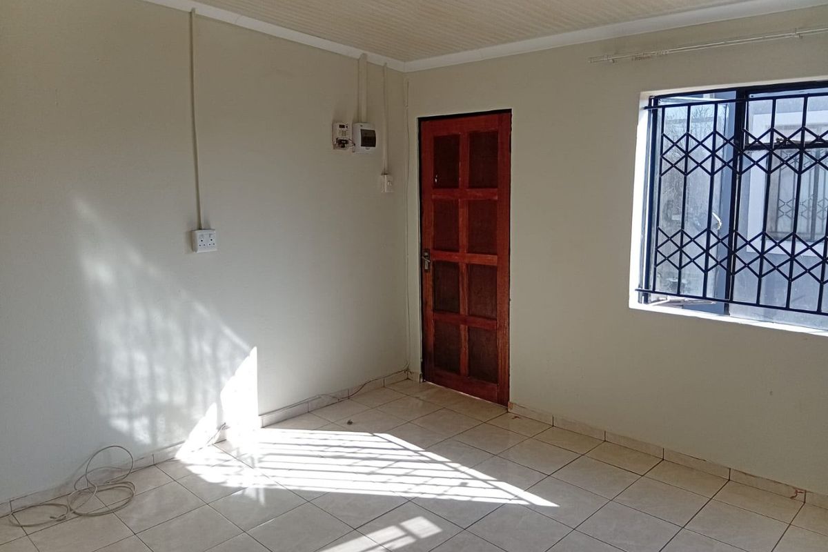 An empty living room featuring tiled flooring, a wooden door, and a window fitted with a security gate.