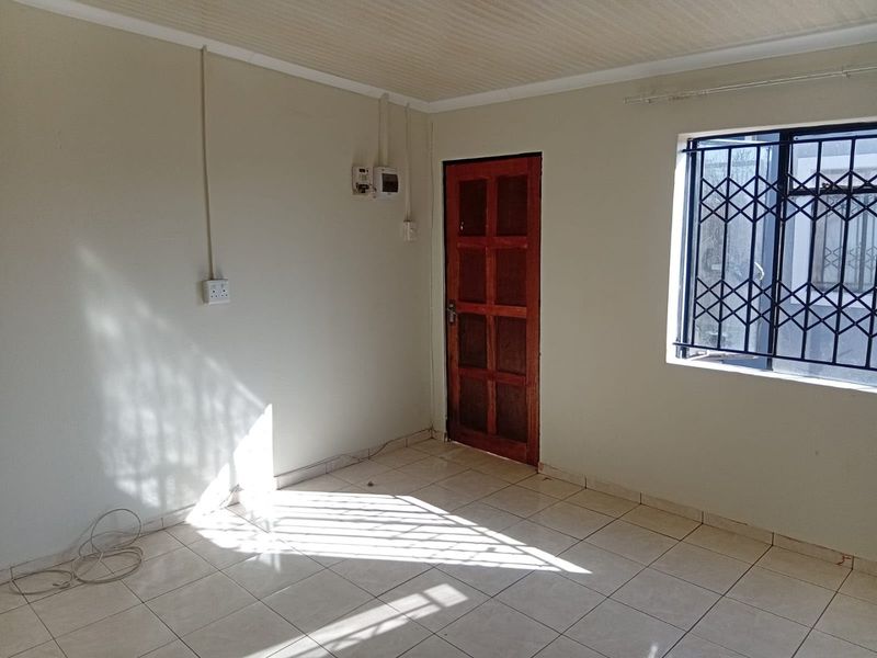 An empty living room featuring tiled flooring, a wooden door, and a window fitted with a security gate.