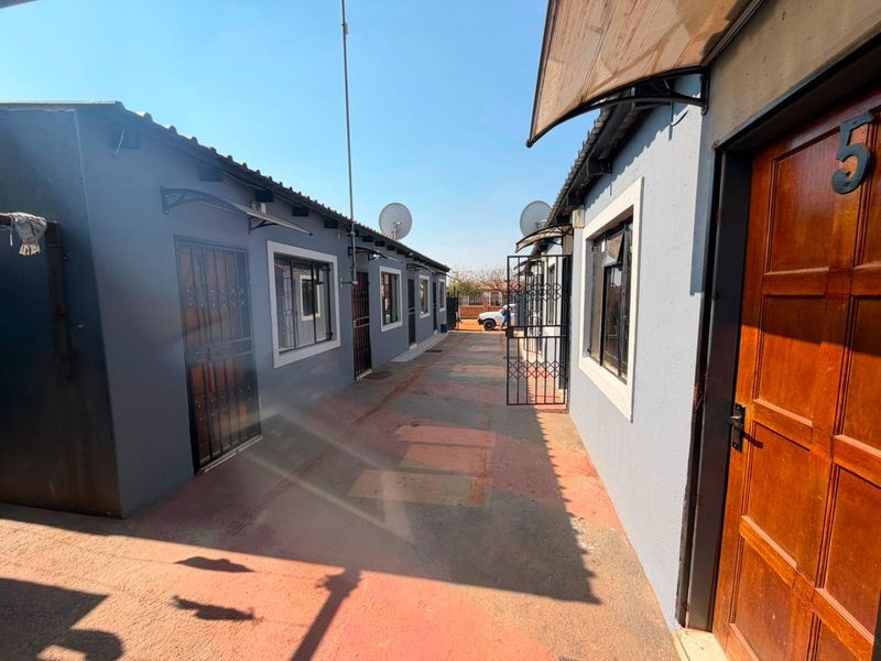 A narrow paved exterior walkway between two residential units featuring security gates, satellite dishes, and external doors.