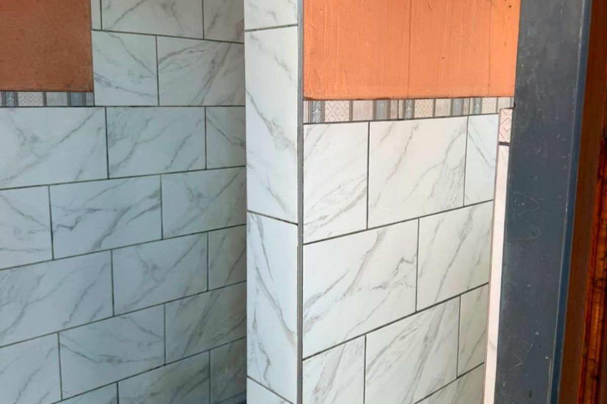 A partially finished shower enclosure featuring marble-look wall tiles and a tiled base, requiring final touches to complete the installation.