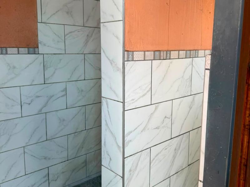 A partially finished shower enclosure featuring marble-look wall tiles and a tiled base, requiring final touches to complete the installation.