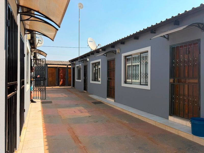 Exterior view of a residential property featuring a paved walkway, multiple unit entrances with security gates, and satellite dish installations.