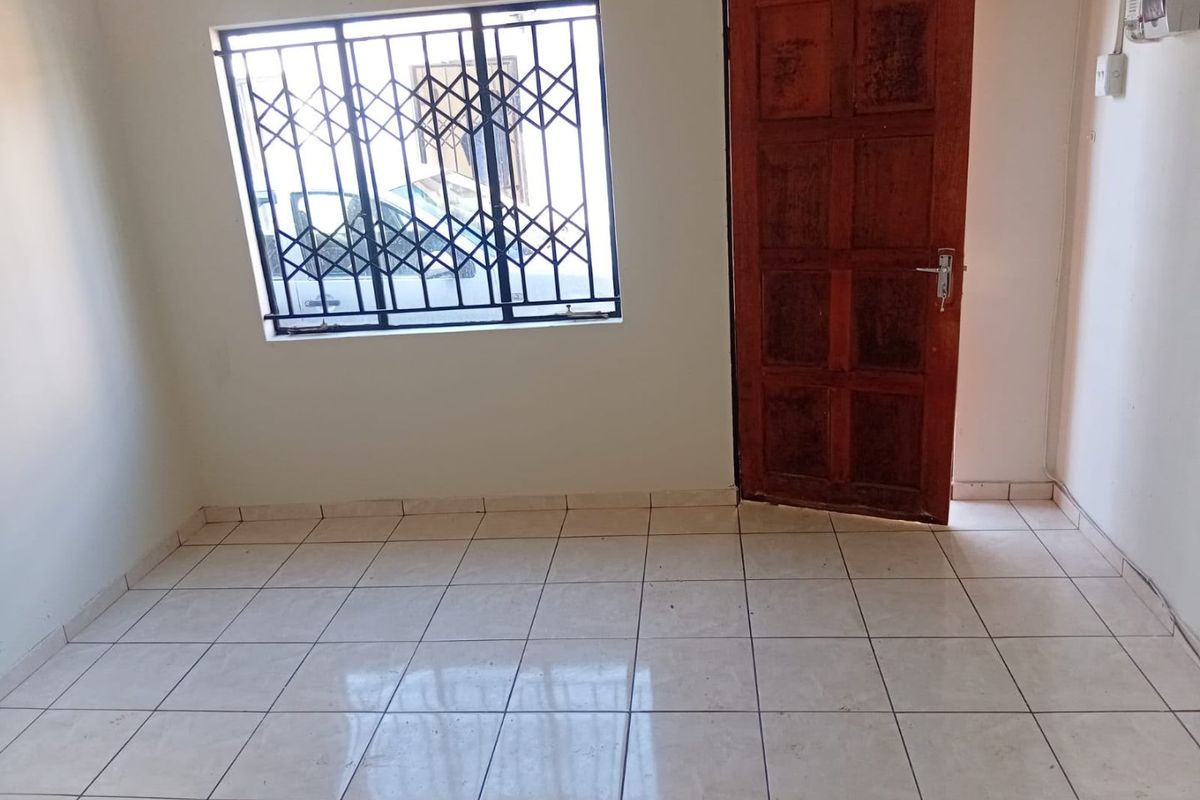 An empty bedroom featuring tiled flooring, a timber door, and a window fitted with a security gate.