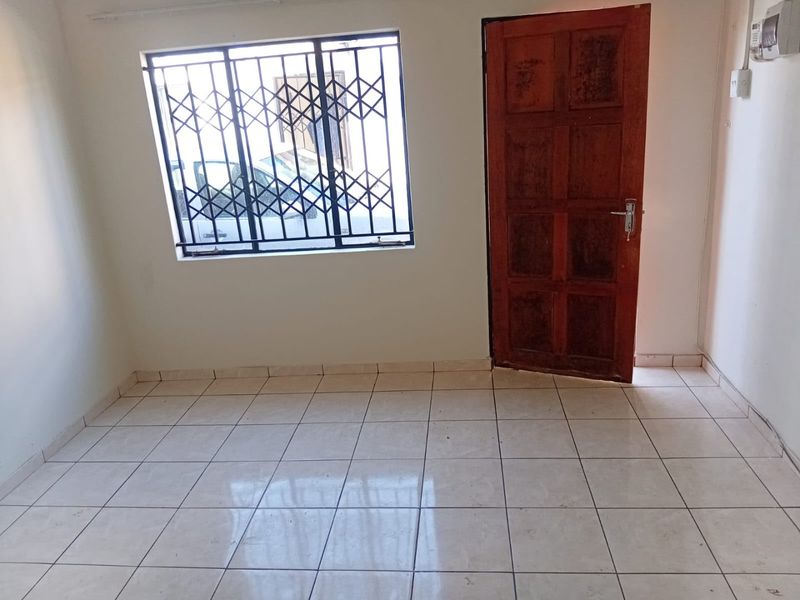 An empty bedroom featuring tiled flooring, a timber door, and a window fitted with a security gate.