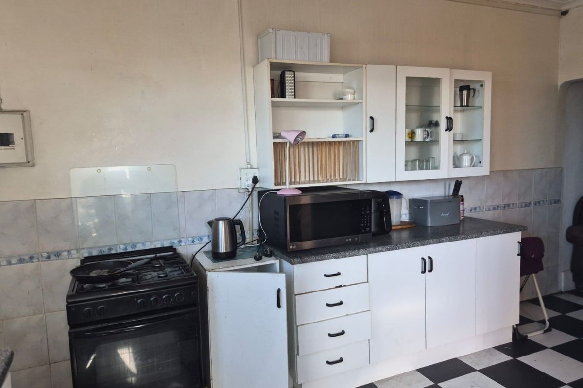 A functional kitchen area featuring a gas stove, built-in white cabinetry, tiled backsplash, and a classic black and white checkered floor.