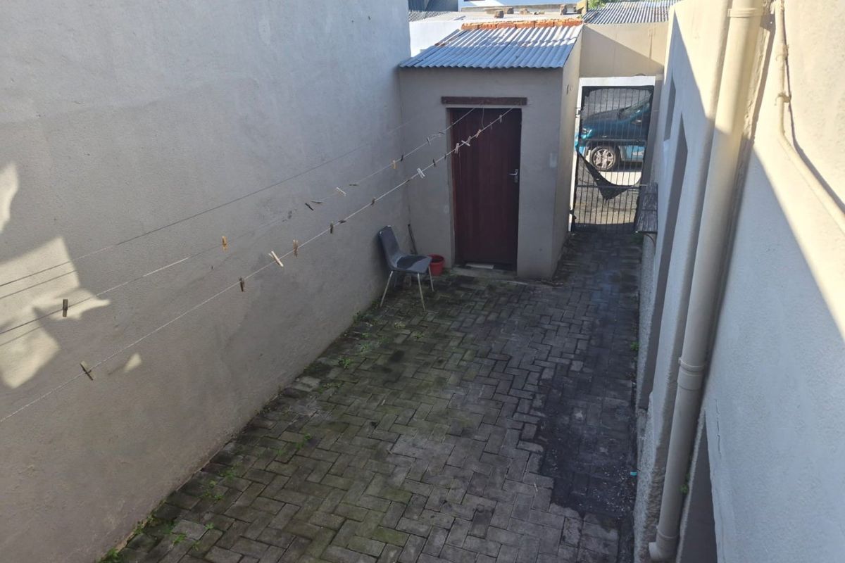A narrow rear courtyard featuring paved flooring, a small utility structure with a corrugated roof, and a metal security gate.
