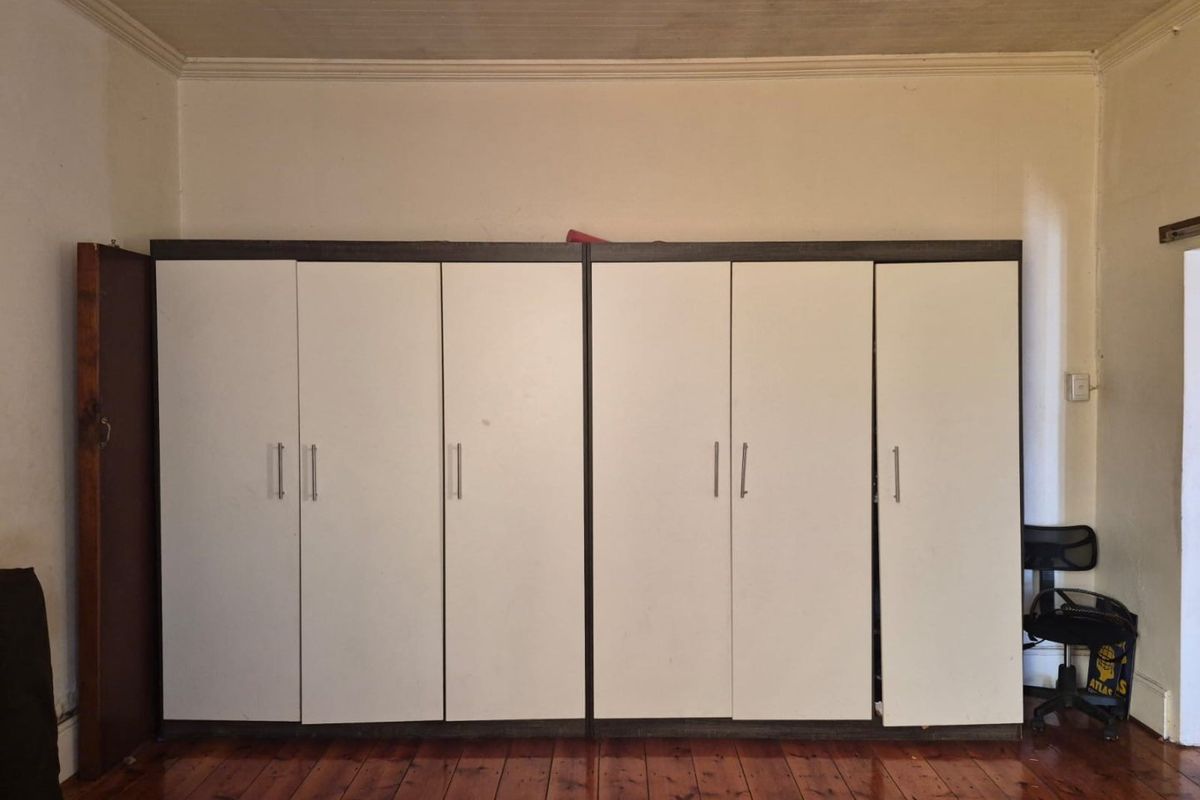 Bedroom featuring extensive built-in storage cupboards, original timber flooring, and a coved ceiling, offering a functional space with potential for cosmetic updates.