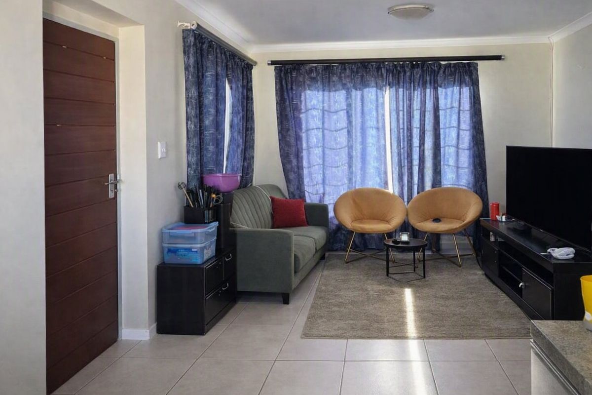 A functional living room featuring neutral tiled flooring, a sliding glass door with curtains, and standard ceiling finishes.