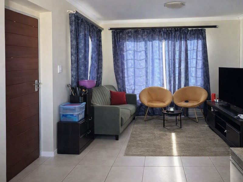 A functional living room featuring neutral tiled flooring, a sliding glass door with curtains, and standard ceiling finishes.