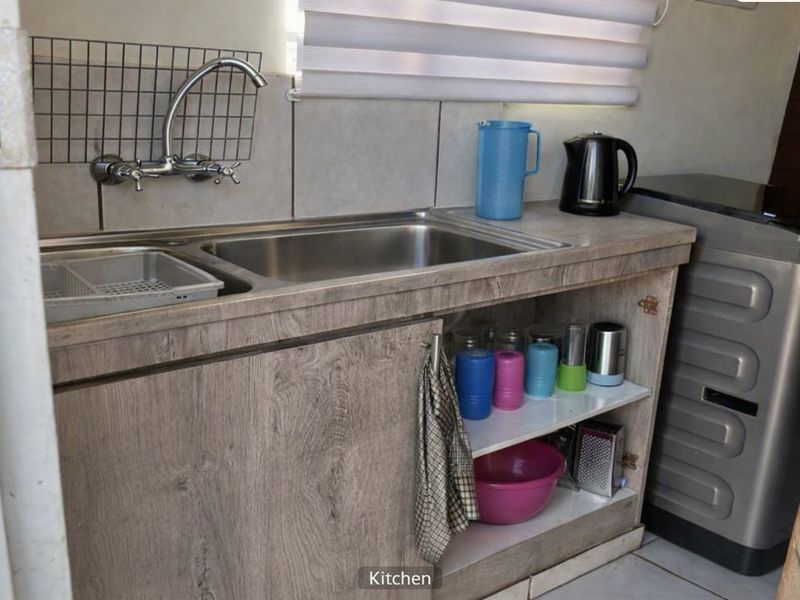 A compact kitchen area featuring a stainless steel sink, wood-look laminate cabinetry, and a tiled backsplash.