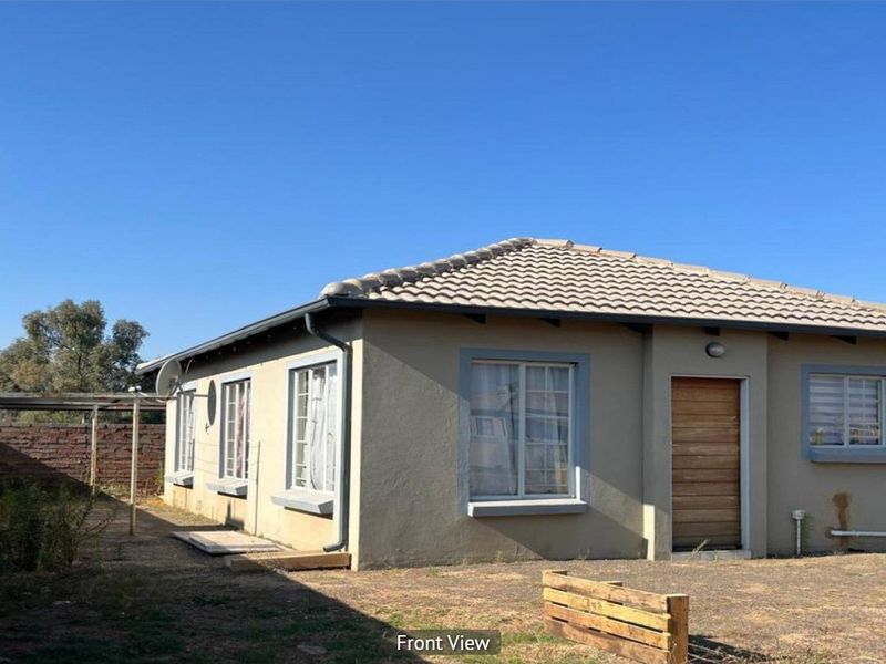 A detached single-story house featuring a tiled roof, timber front door, and a surrounding brick boundary wall on a spacious plot.