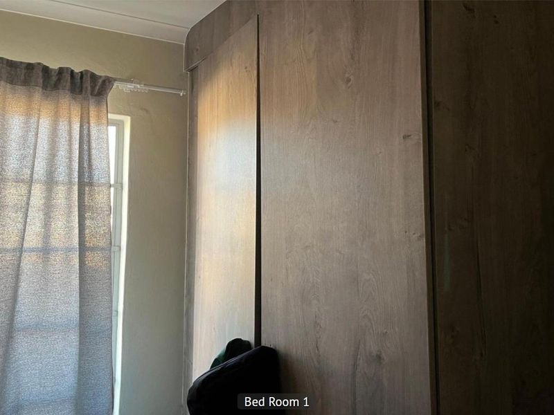A bedroom featuring built-in wooden cupboards and a window with curtains.
