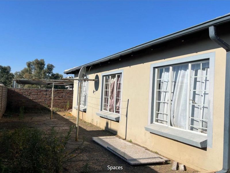Rear exterior view of the property featuring a brick boundary wall, security-barred windows, and a basic garden area with a metal washing line.