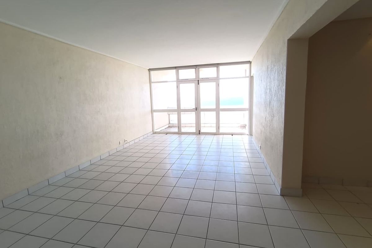 An empty, open-plan living area featuring white tiled flooring and a large glass door providing natural light and access to the exterior.