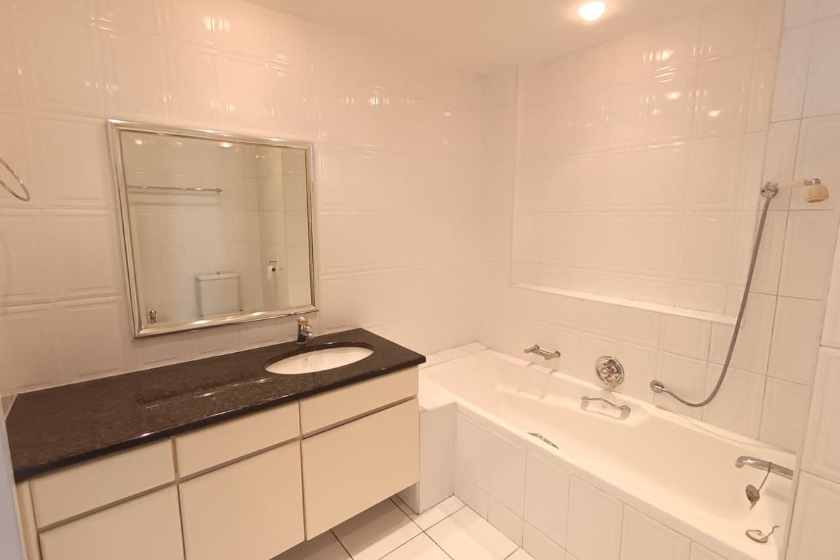 A clean, neutral bathroom featuring a granite-topped vanity, built-in bathtub with handheld shower attachment, and full-height wall tiling.