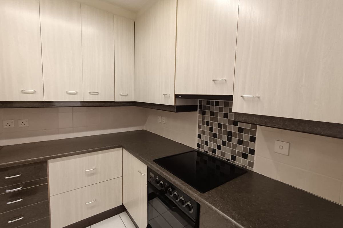 A functional kitchen featuring light wood-look cabinetry, dark countertops, a built-in oven and hob, and a decorative mosaic tile backsplash.