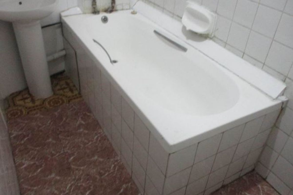 A dated bathroom featuring a pedestal basin and a built-in bathtub with tiled surrounds and flooring, requiring cosmetic updates.