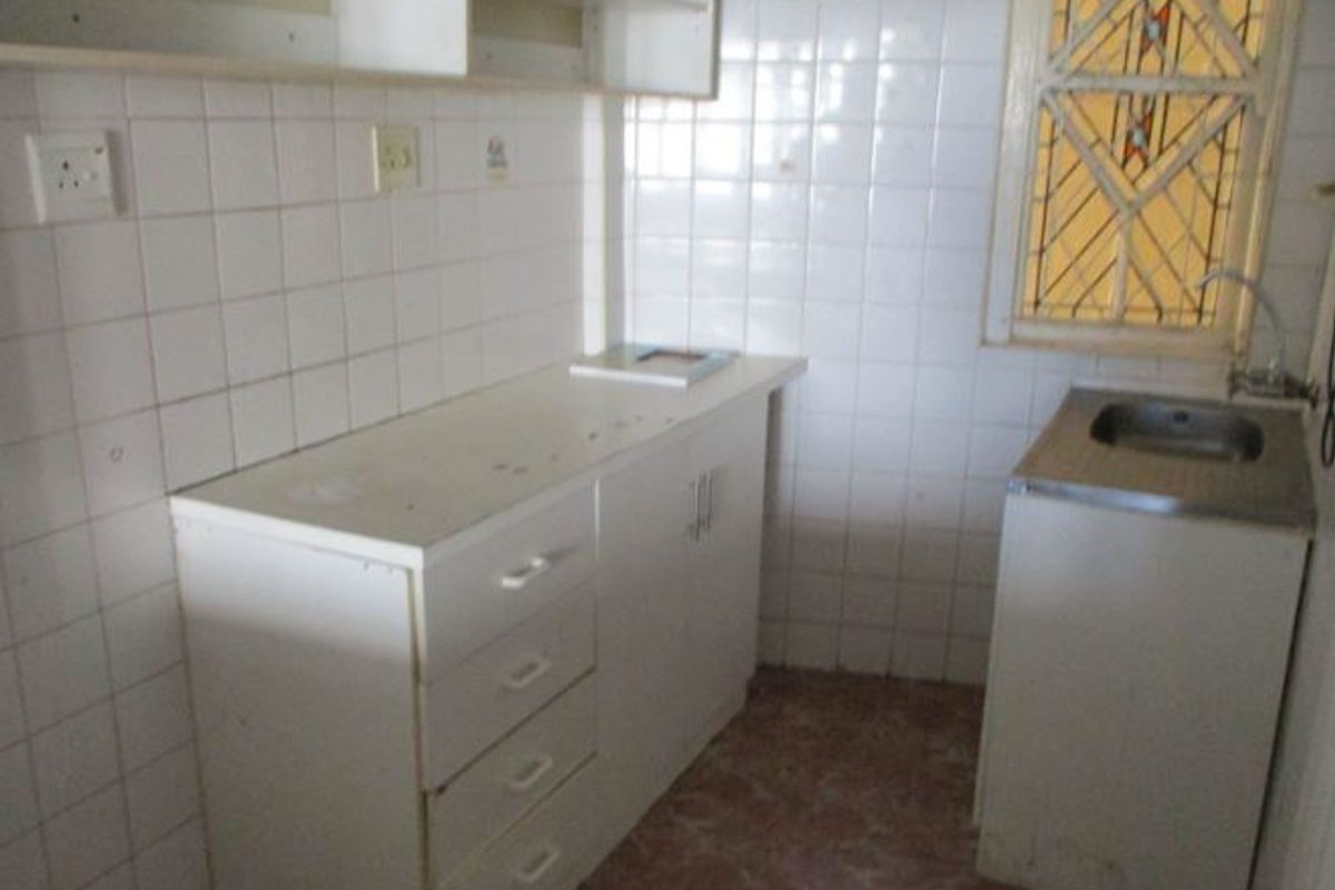 A compact, functional kitchen area featuring built-in white cabinetry, a stainless steel sink, and tiled splashbacks, offering a blank canvas for renovation.