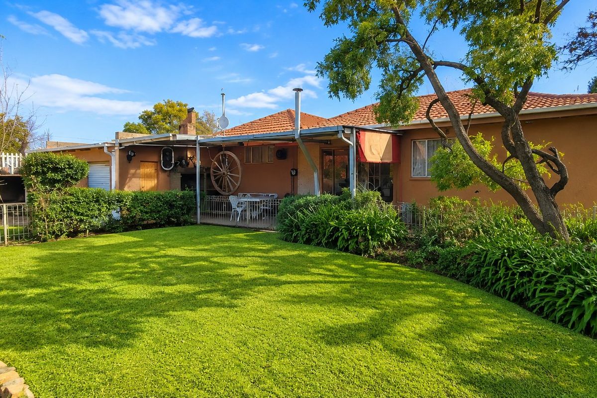 Rear view of the house featuring a well-maintained lawn, a covered patio area, and established garden landscaping.