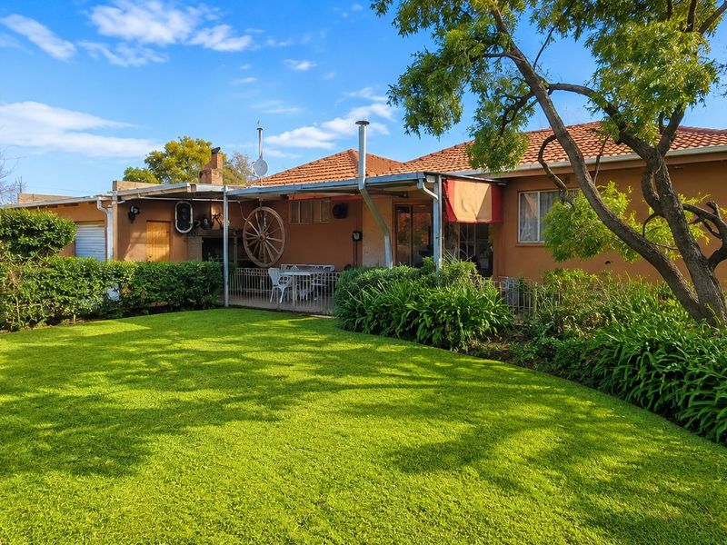 Rear view of the house featuring a well-maintained lawn, a covered patio area, and established garden landscaping.