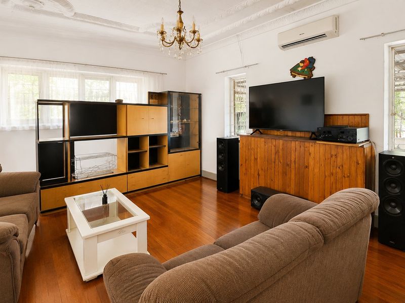A spacious living room featuring polished hardwood flooring, ornate ceiling detailing, and a wall-mounted split-system air conditioner.