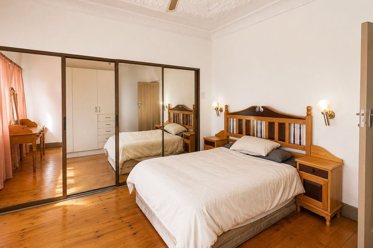 A bedroom featuring polished timber flooring, ornate ceiling detailing, and a large built-in mirrored wardrobe providing ample storage space.