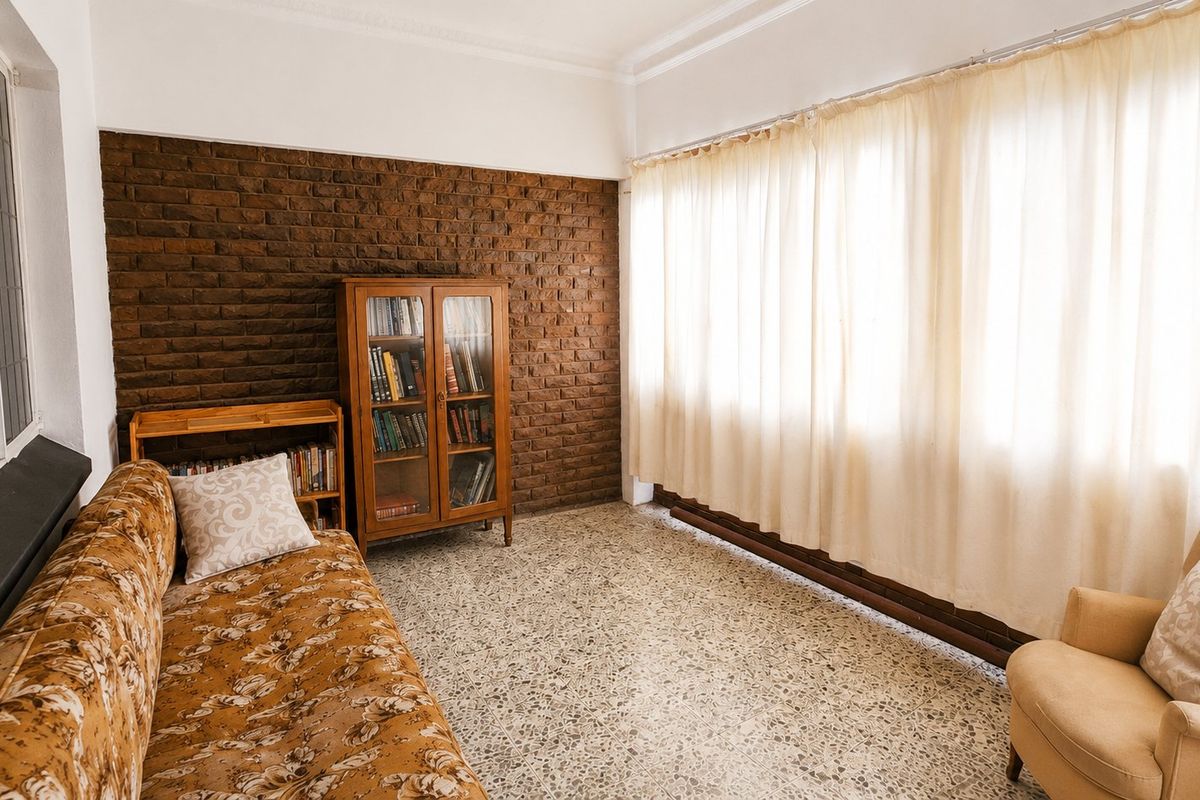A living room featuring a textured exposed brick wall, classic terrazzo flooring, and large windows with natural light.