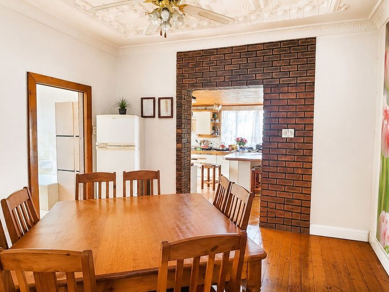 Dining room featuring timber flooring, an ornate ceiling rose, and a distinctive exposed brick archway leading through to the kitchen area.