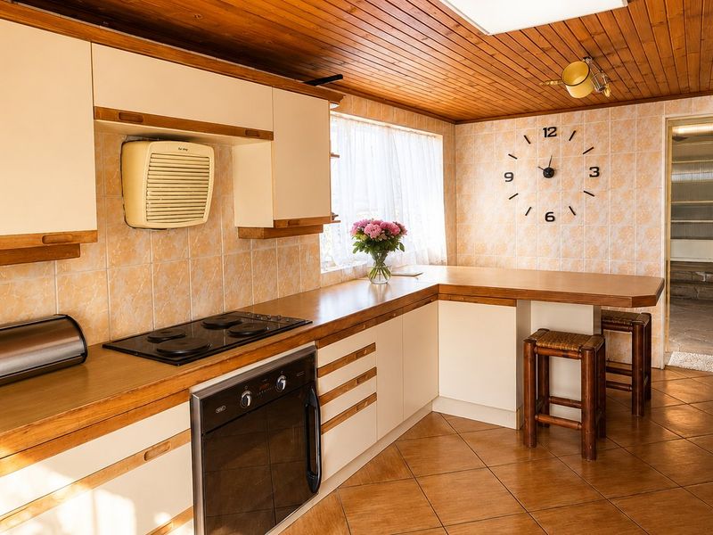 A functional kitchen featuring built-in cabinetry, an integrated oven and hob, tiled splashbacks, and a timber-clad ceiling with a breakfast bar area.