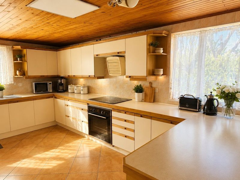 Spacious kitchen featuring timber ceiling, ample cabinetry, integrated oven, electric cooktop, and large windows providing natural light.