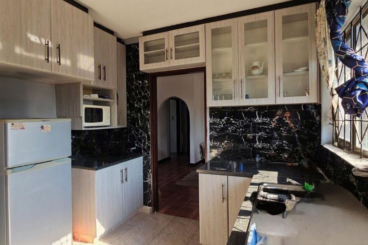 A functional kitchen featuring light wood-grain cabinetry, contrasting black marble-effect splashbacks, and ample storage space with glass-fronted upper cabinets.