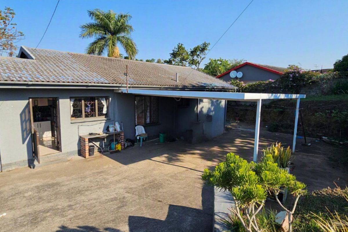 Rear view of the house featuring a concrete patio area, a covered carport, and a built-in brick braai station.