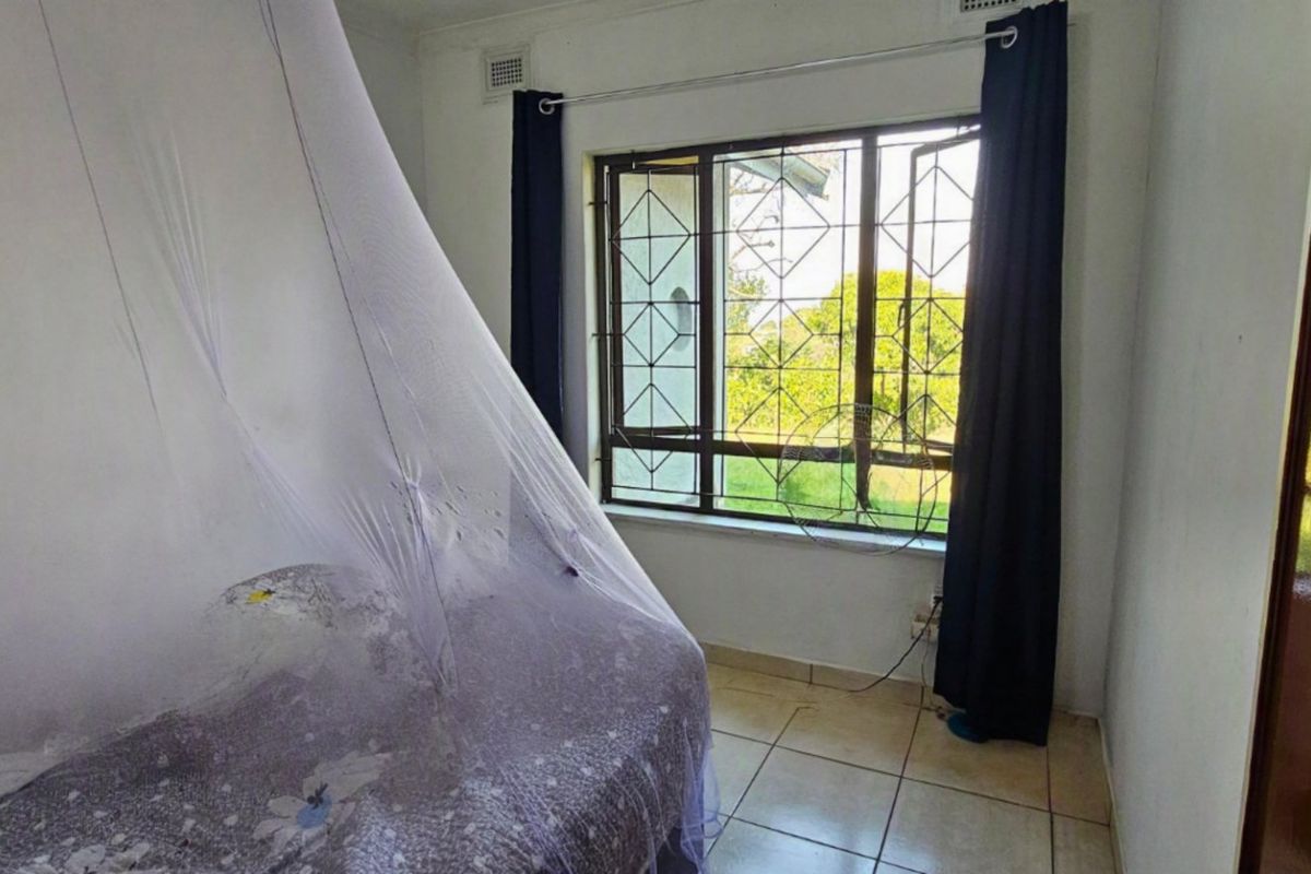 A bedroom featuring tiled flooring and a window fitted with a security gate, offering a view of the garden area.