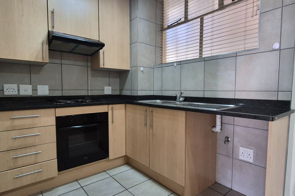 A functional kitchen featuring light wood cabinetry, granite countertops, a built-in oven, gas hob, and tiled finishes throughout.