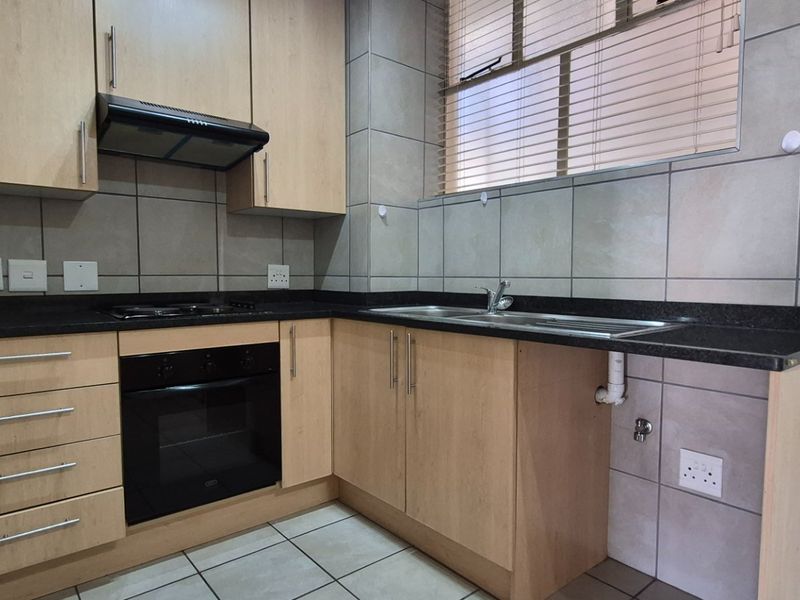 A functional kitchen featuring light wood cabinetry, granite countertops, a built-in oven, gas hob, and tiled finishes throughout.