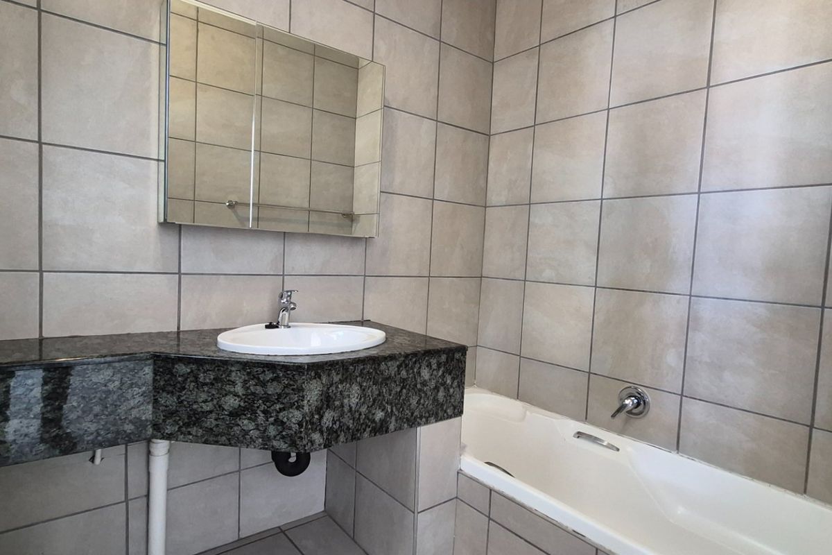 A clean, tiled bathroom featuring a granite vanity top with an integrated sink, a wall-mounted medicine cabinet, and a standard bathtub.