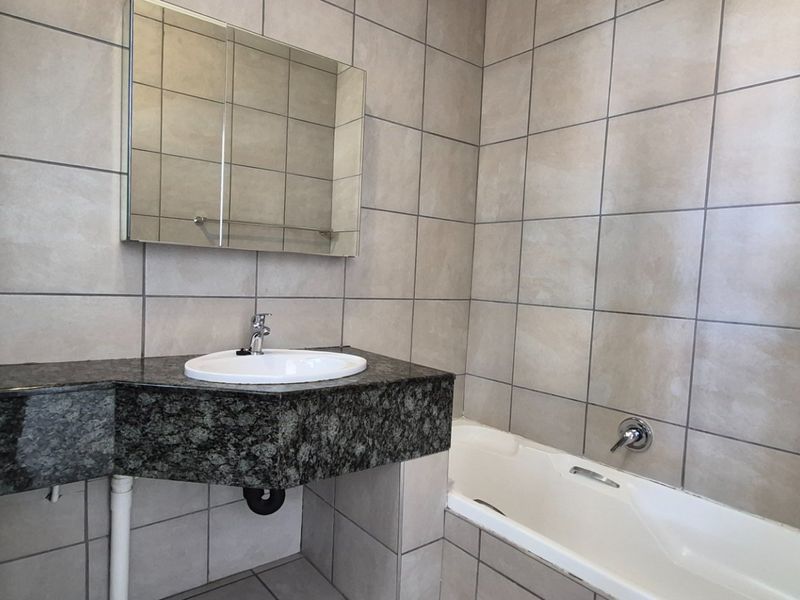 A clean, tiled bathroom featuring a granite vanity top with an integrated sink, a wall-mounted medicine cabinet, and a standard bathtub.