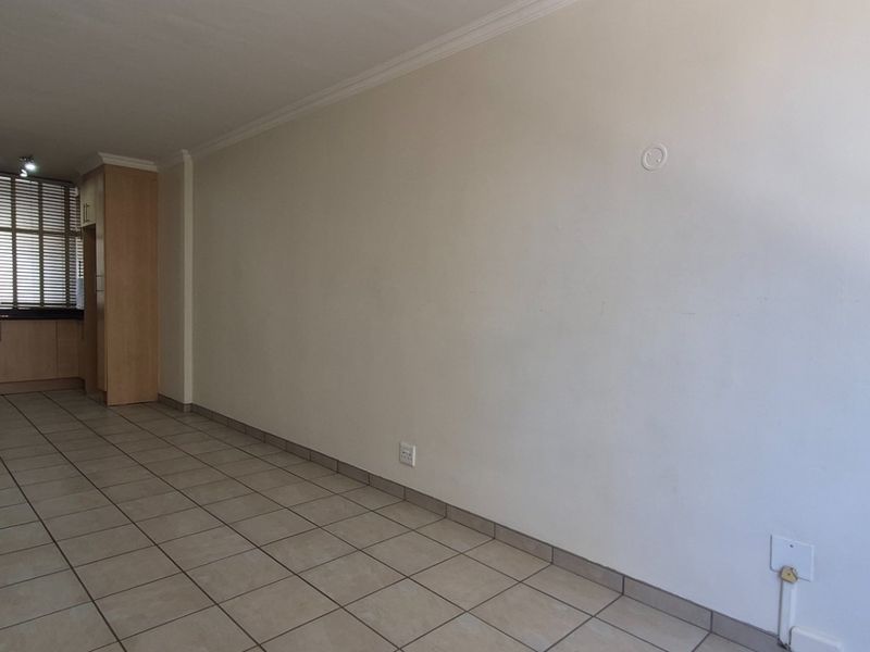 An empty open-plan living area featuring tiled flooring, neutral walls, and built-in cabinetry near the entrance.
