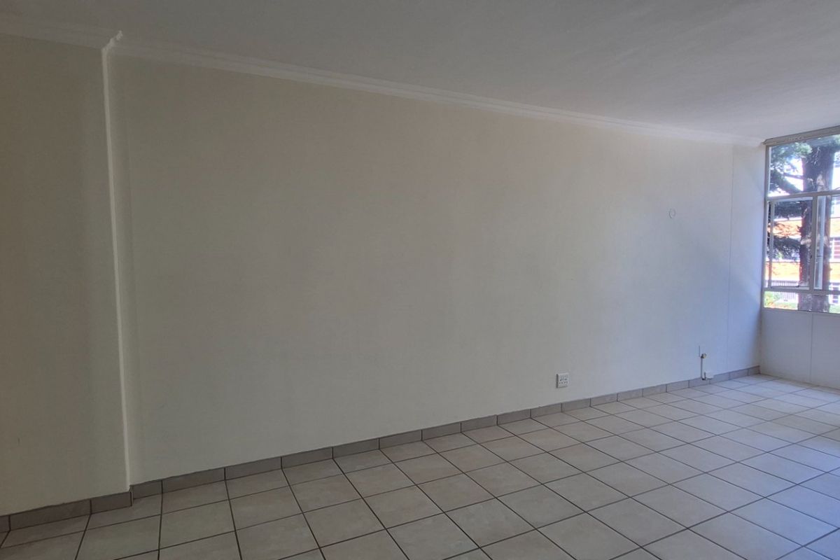A bright, empty living area featuring neutral tiled flooring, a large window providing natural light, and a built-in cupboard for storage.