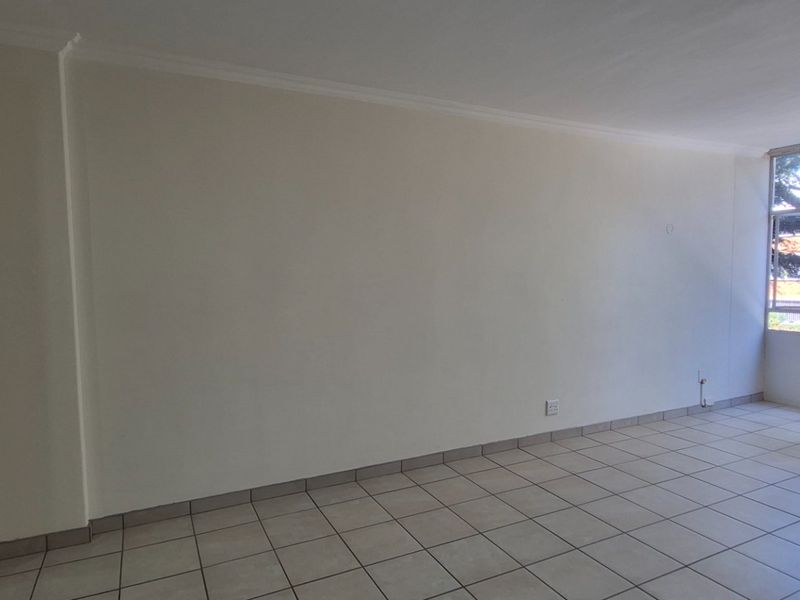 A bright, empty living area featuring neutral tiled flooring, a large window providing natural light, and a built-in cupboard for storage.